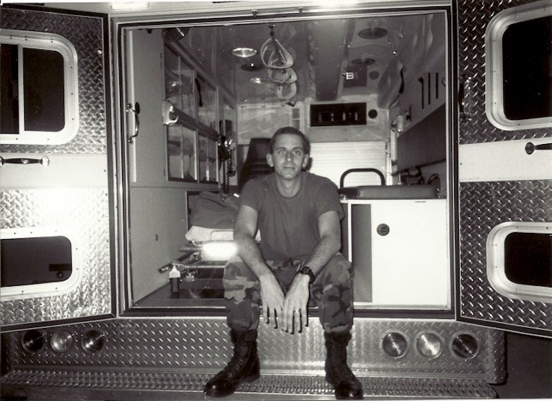 A man seated in the back of an ambulance, appearing calm and attentive to his surroundings.